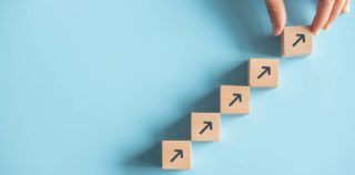Close up man hand arranging wood block stacking as step stair on paper pink background. Business concept growth success process, copy space. Le transfert des contrats de travail continue de nourrir la jurisprudence