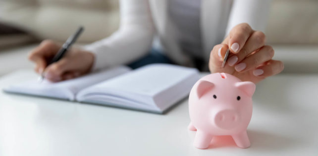 Thrifty woman sit at table hold pen writing daily expenses in diary put coin in pink piggy bank close up. Saving money for future, caring for tomorrow, makes stash of cash, investment, economy concept Supplément de participation ou d’intéressement : la Cour de cassation sème le trouble