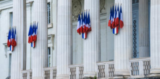 Sturdy white columns adorned with French flags guard the front facade of the Palace of Justice in Tours, France. Quand l’abus de droit s’efface devant la logique de groupe