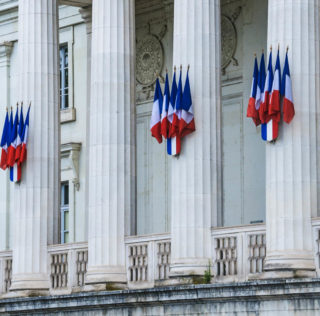 Sturdy white columns adorned with French flags guard the front facade of the Palace of Justice in Tours, France. Quand l’abus de droit s’efface devant la logique de groupe