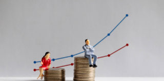 The concept of gender pay gap. A miniature man and a miniature woman sitting on top of a pile of coins at different heights in front of a bar graph. Ecarts de représentation entre les femmes et les hommes : quelles informations doivent être transmises au ministère du Travail ?