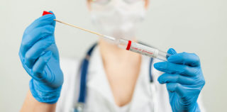 Test for coronavirus Covid-19. Female doctor or nurse doing lab analysis of a nasal swab in a hospital laboratory. Medical technologist holding a COVID-19 smear kit, wearing protective gloves from Le coût des tests de dépistage n’est pas un frais professionnel