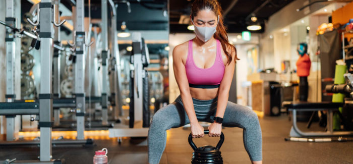A female athlete is wearing a protective face mask and lifting a kettlebell in a gym. Mise à disposition d’une salle de sport dans l’entreprise : est-ce un avantage en nature soumis aux cotisation sociales ?