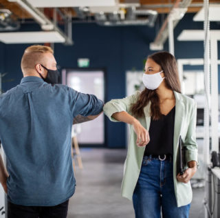 Two business colleagues greeting with elbow in office. Business people bump elbows in office for greeting during covid-19 pandemic. Covid-19 : les salariés vulnérables continueront à bénéficier de l’activité partielle