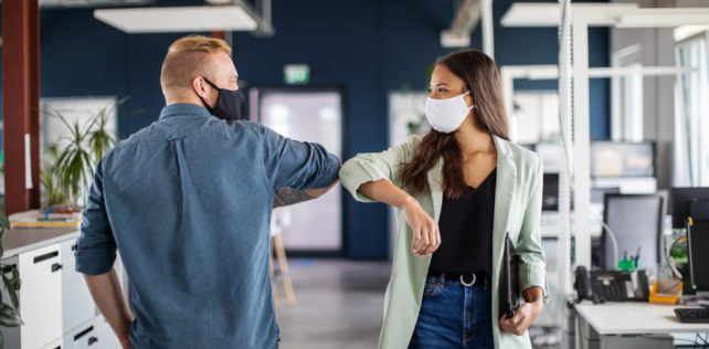 Two business colleagues greeting with elbow in office. Business people bump elbows in office for greeting during covid-19 pandemic. Covid-19 : les salariés vulnérables continueront à bénéficier de l’activité partielle