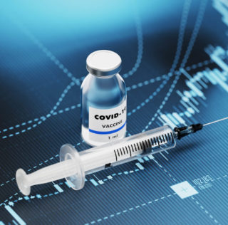 COVID-19 vaccine and syringe sitting over blue financial graph background. Selective focus. Horizontal composition with copy space. COVID-19 Vaccine and Stock market and finance concept. Covid-19 : renforcement des outils de gestion de la crise sanitaire