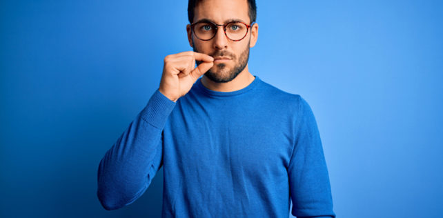 Young handsome man with beard wearing casual sweater and glasses over blue background mouth and lips shut as zip with fingers. Secret and silent, taboo talking; Shutterstock ID 1748856581; ordering_party: CMS LS; job_project: 21_0004_040 / The Economist / Image Concept / IP; purchase_order: Hans Scholten Licenciement pour divergence de vue : attention à la nullité du licenciement pour atteinte à la liberté d’expression du salarié