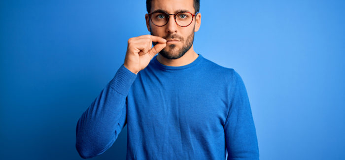 Young handsome man with beard wearing casual sweater and glasses over blue background mouth and lips shut as zip with fingers. Secret and silent, taboo talking; Shutterstock ID 1748856581; ordering_party: CMS LS; job_project: 21_0004_040 / The Economist / Image Concept / IP; purchase_order: Hans Scholten Licenciement pour divergence de vue : attention à la nullité du licenciement pour atteinte à la liberté d’expression du salarié
