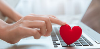 Hand touching red heart on laptop keyboard for flirt love chat or lover online text messenger for find date couple during stay home Coronavirus pandemic situation Ne pas informer son employeur d’une relation intime avec un autre salarié peut justifier un licenciement disciplinaire