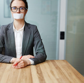 Voiceless busineswoman with her mouth stuck sitting by workplace Entretien préalable : faut-il informer le salarié de son droit de se taire ?