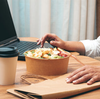 a woman is working on a laptop at home, there is food on the table, salad, coffee and juice, delivery, work at home, La Cour de cassation consacre le droit des télétravailleurs aux titres-restaurant au nom du principe d’égalité de traitement